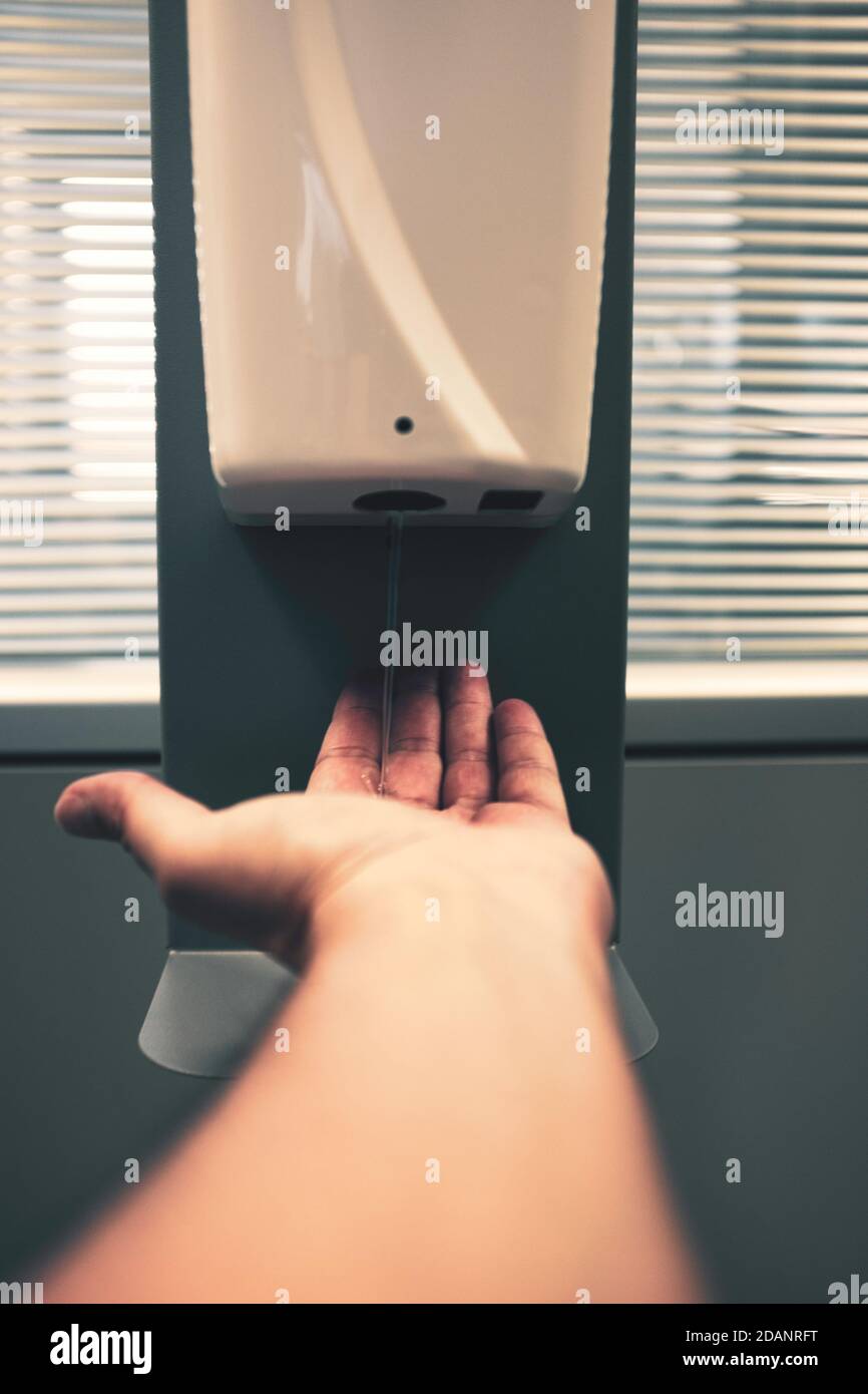 Male hand using automatic alcohol dispenser for cleaning hands in the office or hospital to sanitize virus and bacteria - Infection prevention concept Stock Photo