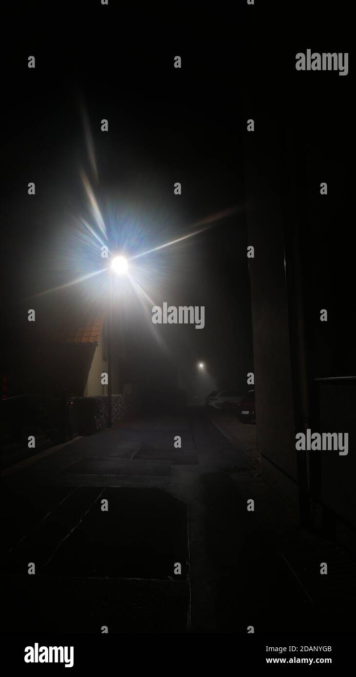 A painful light is shining in a narrow street like an alien UFO during night and the corona pandemics Stock Photo