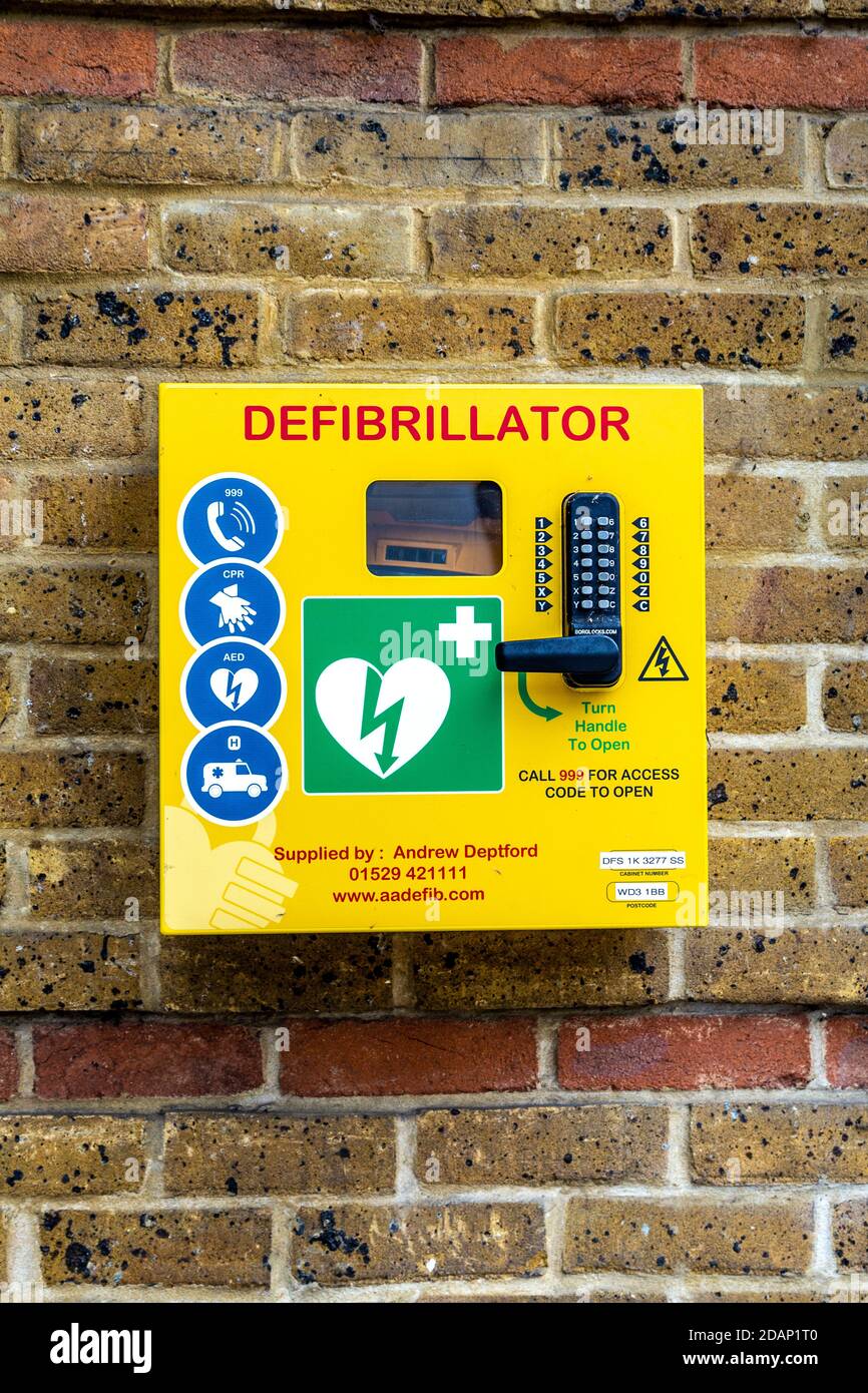 Yellow defibrillator box attached to a brick wall, Rickmansworth, UK