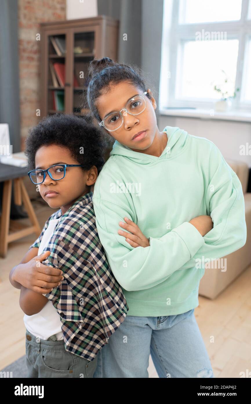 Two mixed-race siblings in casualwear and eyeglasses crossing arms on chest Stock Photo