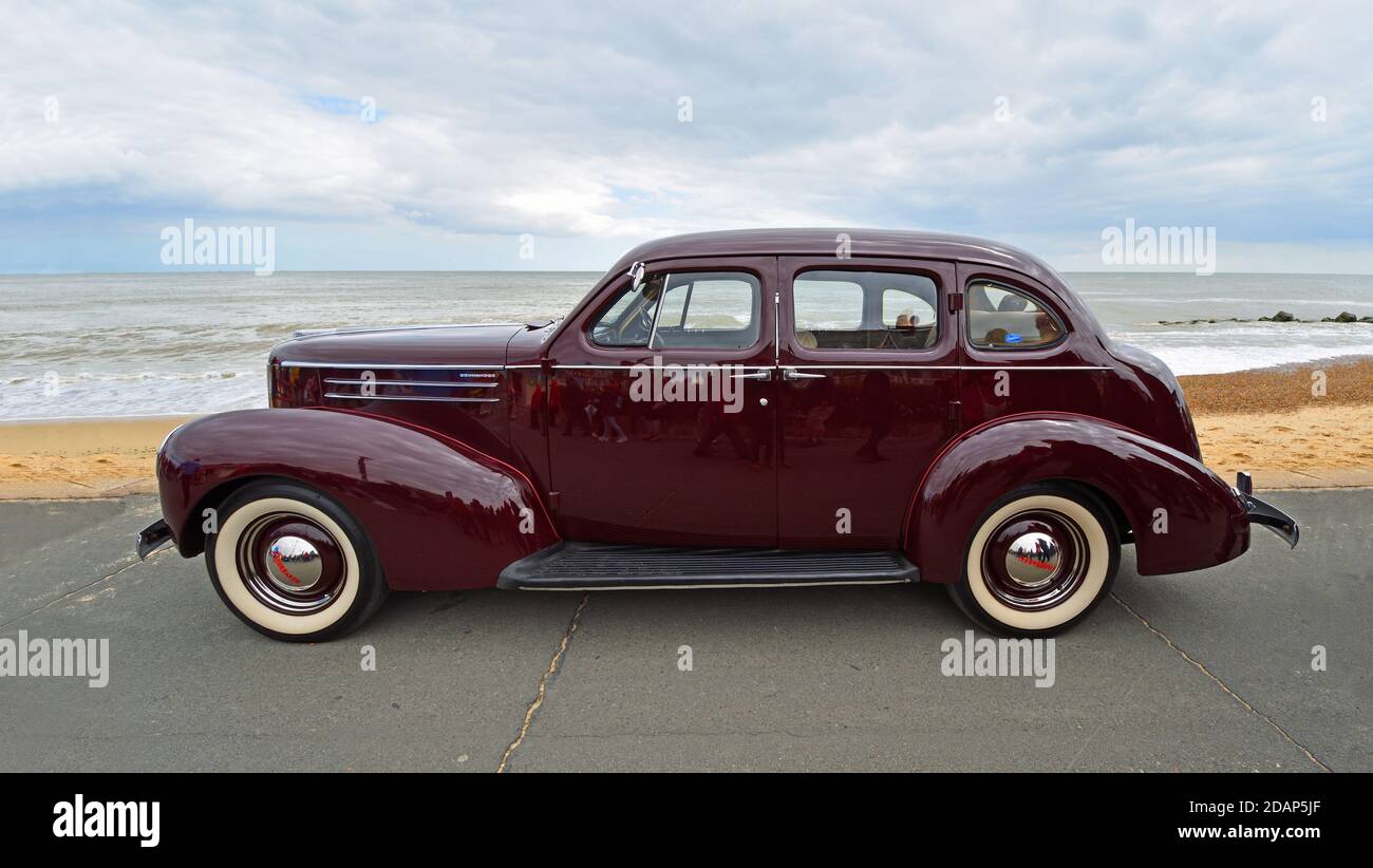 Classic Dark Red Studebaker  motor car parked  on seafront promenade beach and sea in background. Stock Photo