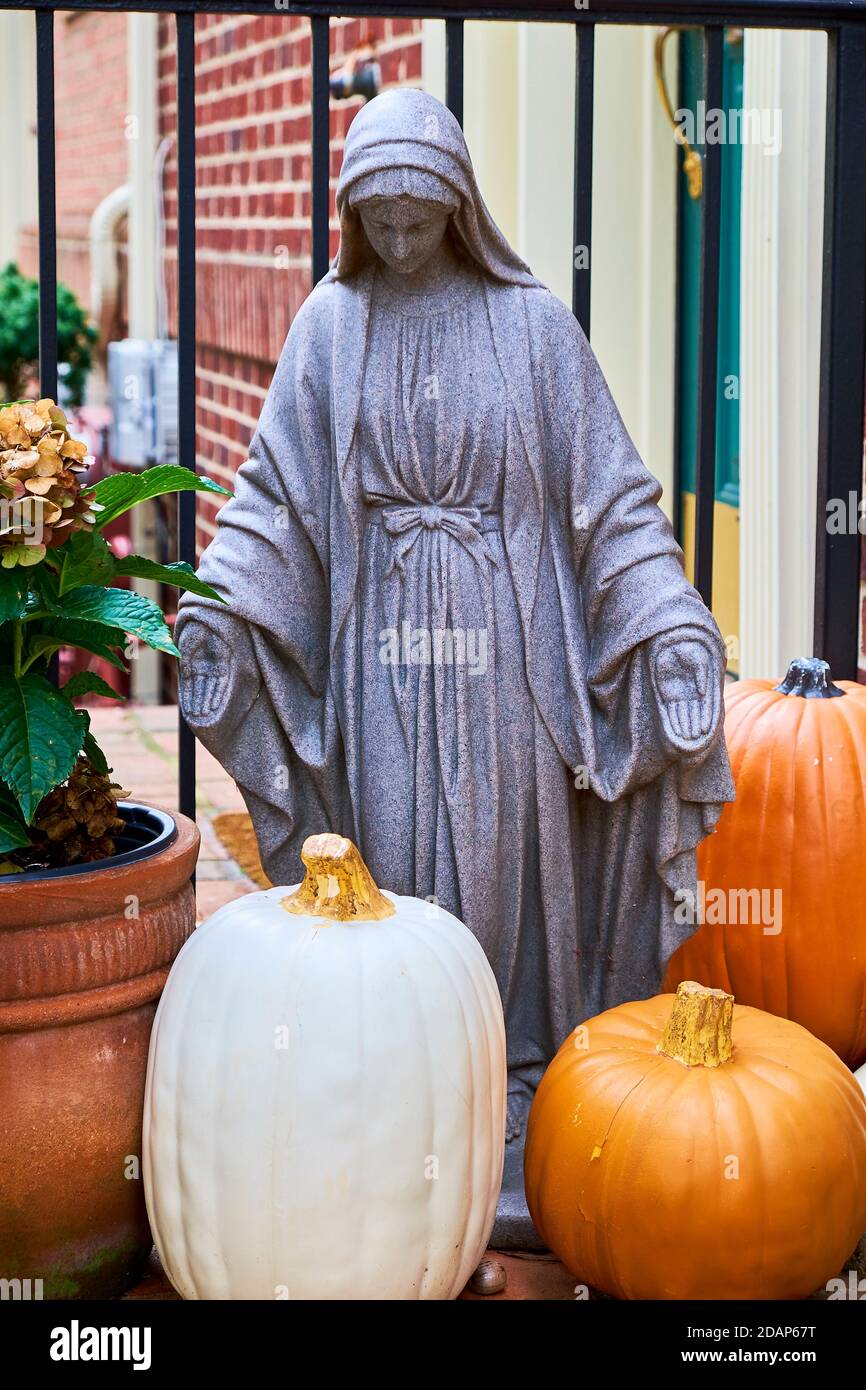 A funny juxtaposition of a Virgin Mary sculpture with some pumpkins on a front porch during