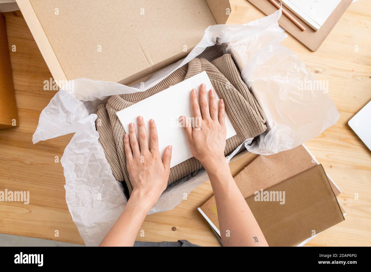 Hands of young manager of online shop putting paper on top of folded sweater Stock Photo