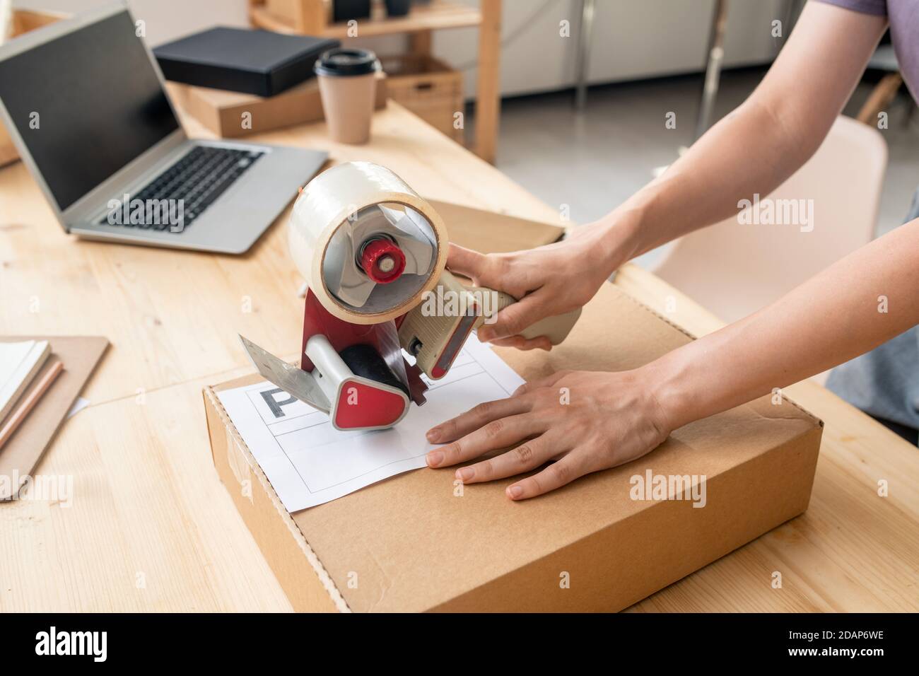 Hands of female manager of online shop sealing cardboard box with packed order Stock Photo