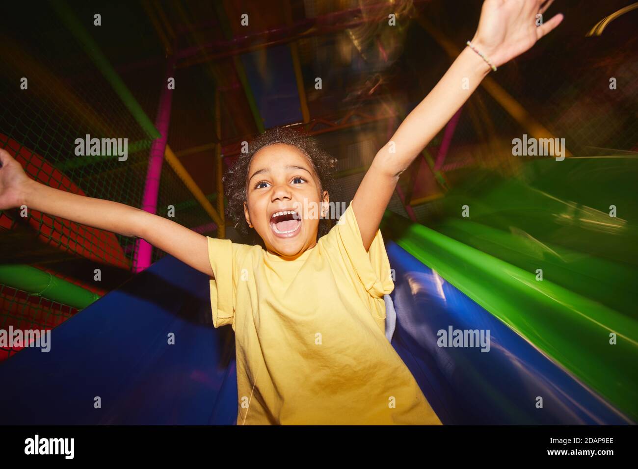Happy African girl riding on a slide she having fun in play center Stock Photo