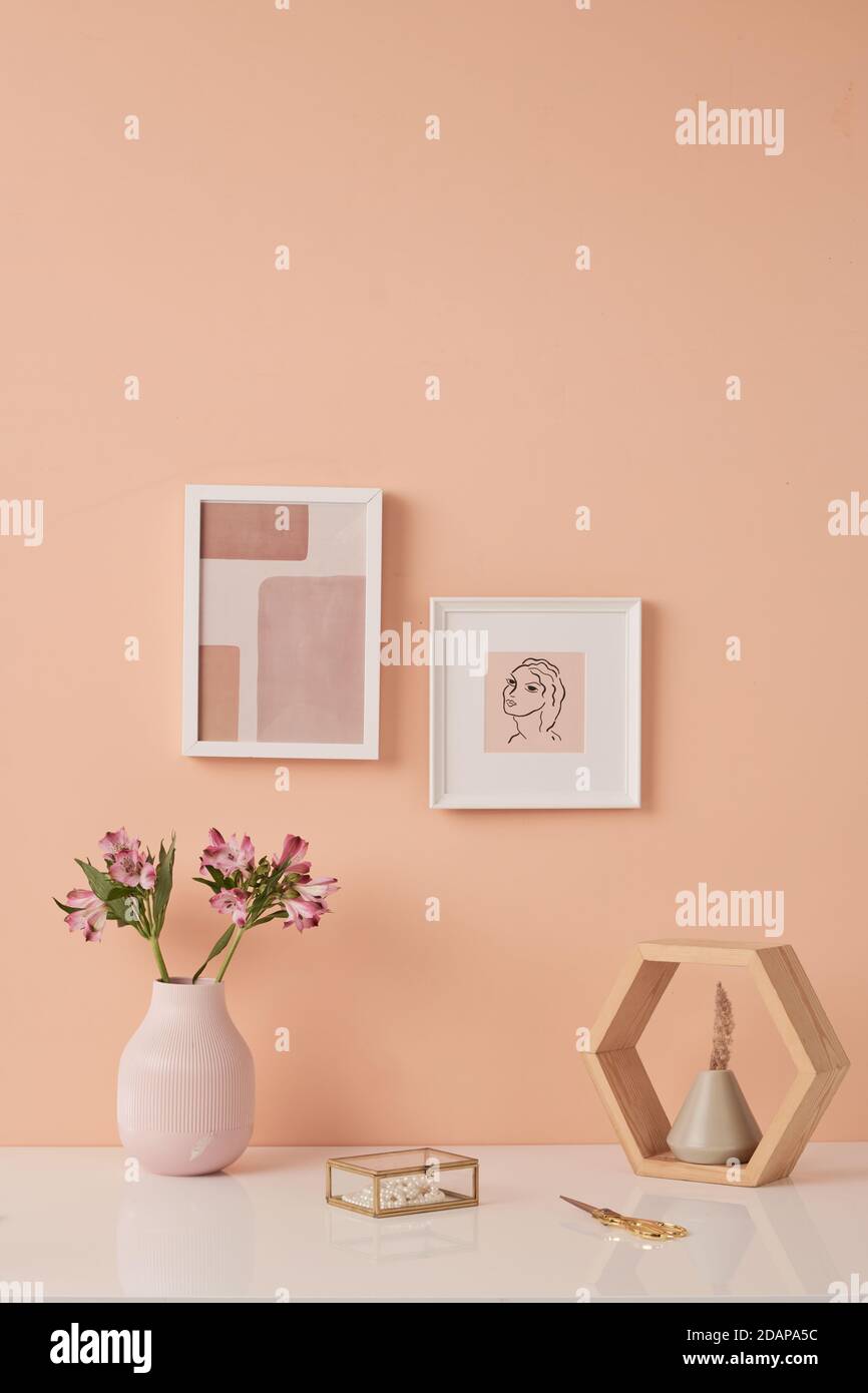 Two pictures in frames on pink wall by table with flowers in white ceramic vases Stock Photo
