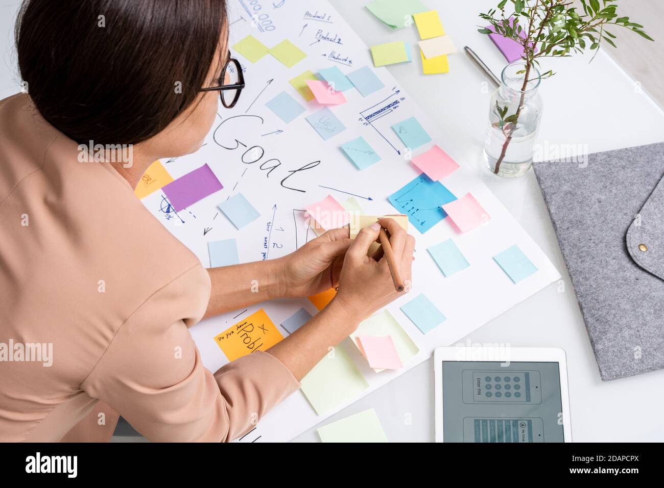 Young brunette businesswoman making notes on notepaper over large document Stock Photo