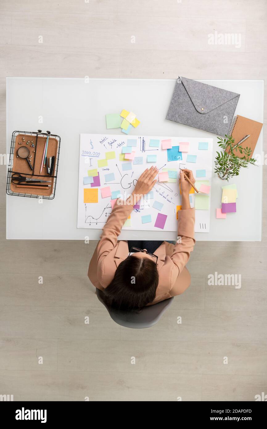 Overview of brunette businesswoman making working notes on notepapers ...
