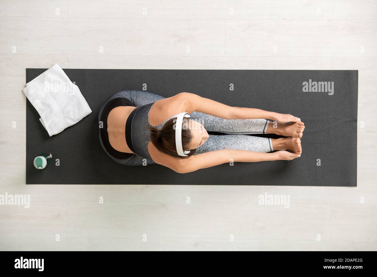 View of young active woman in headphones and tracksuit exercising on mat Stock Photo