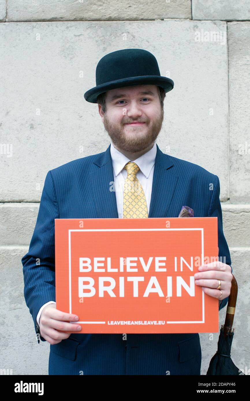 Englishman with bowler hat holds a placard reading  “Believe in Britain” outside the Houses of Parliament, London , UK Stock Photo
