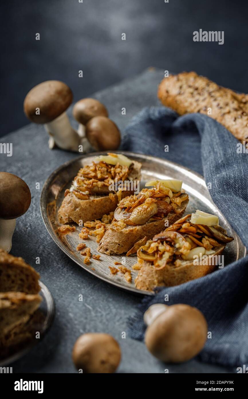 Still life picture of delicious and healthy bruschetta or sandwich with roasted garlic and champignon mushrooms on the blue, textured table Stock Photo