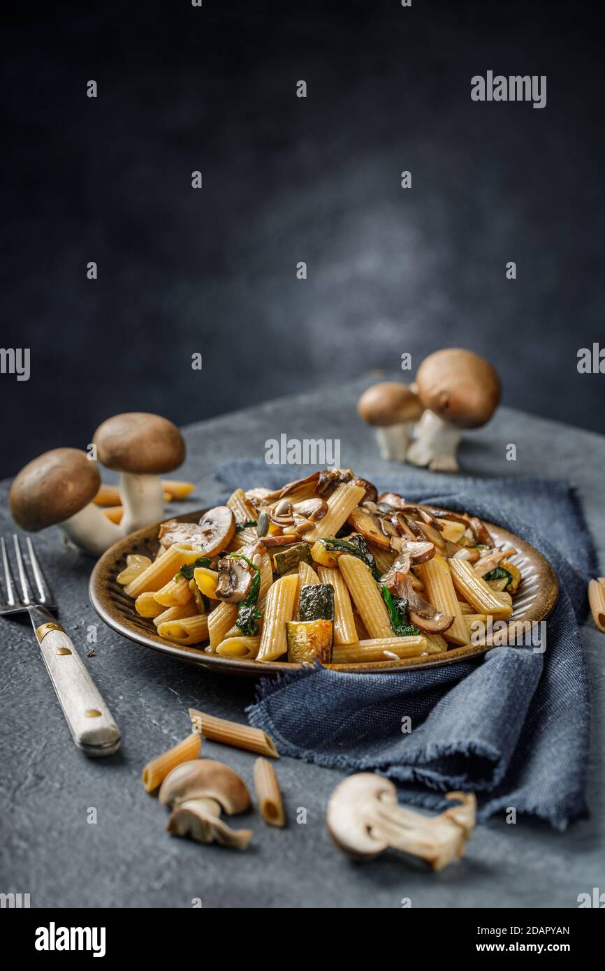 Pasta penne with roasted mushrooms, garlic and zucchini. Italian food on blue marble table. Stock Photo