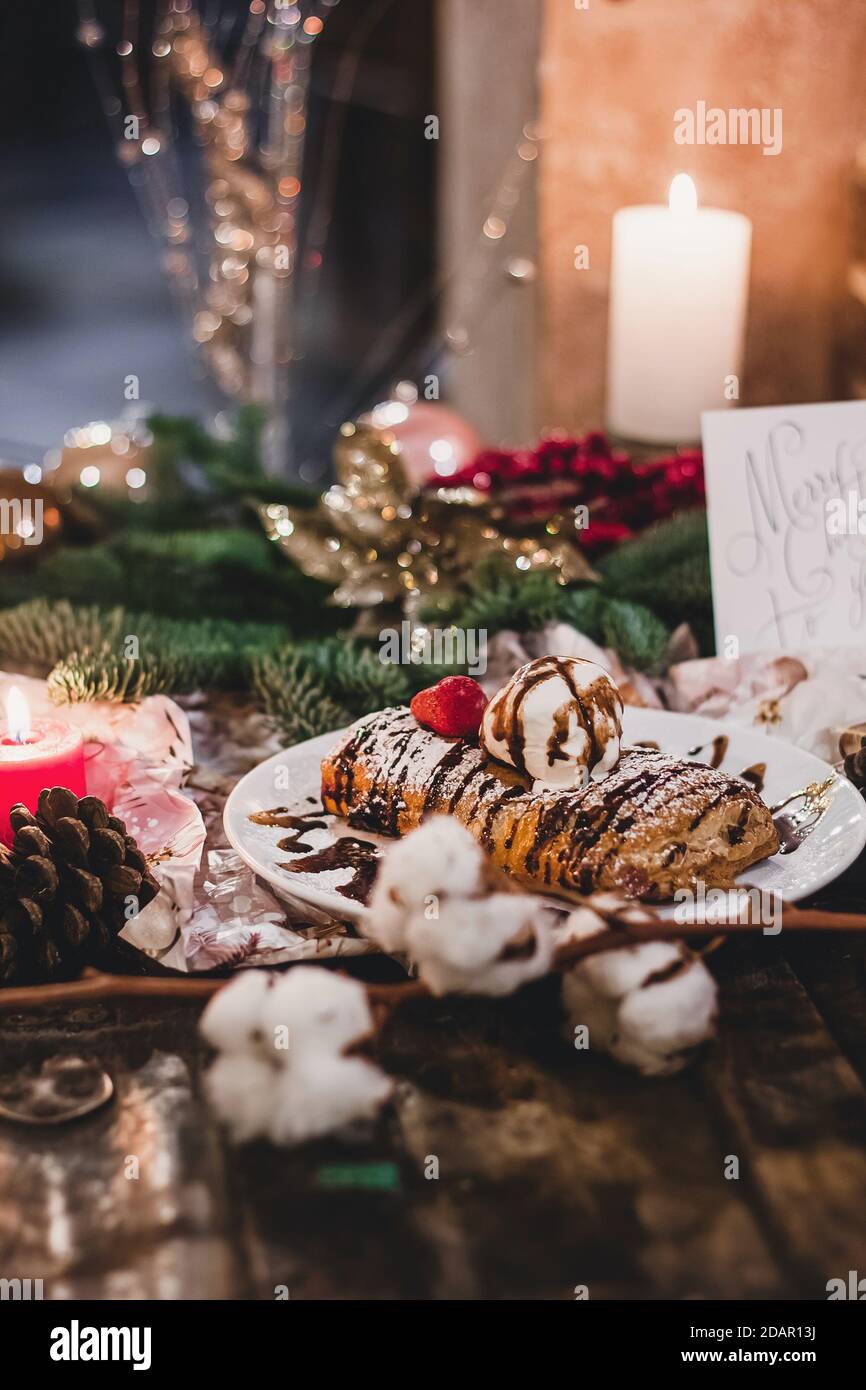 Closeup of a strudel with a strawberry on a Christmas plate near bamboo branch. Christmas breakfast on a wooden table Stock Photo