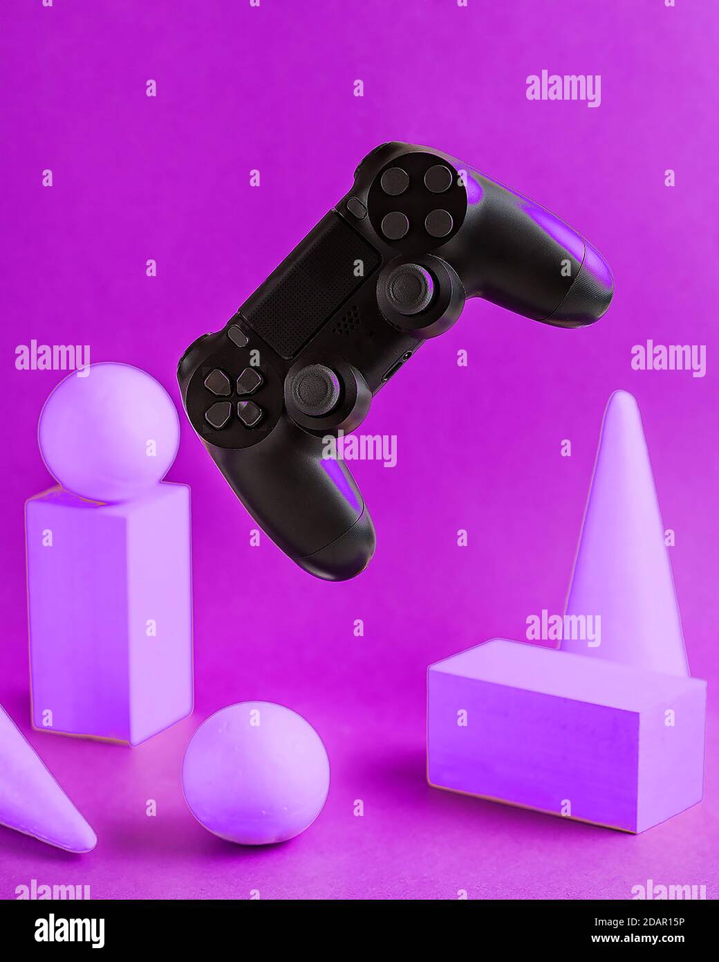 Black game joystick hanging in space, white three-dimensional geometric shapes on a purple background. computer games. Stock Photo