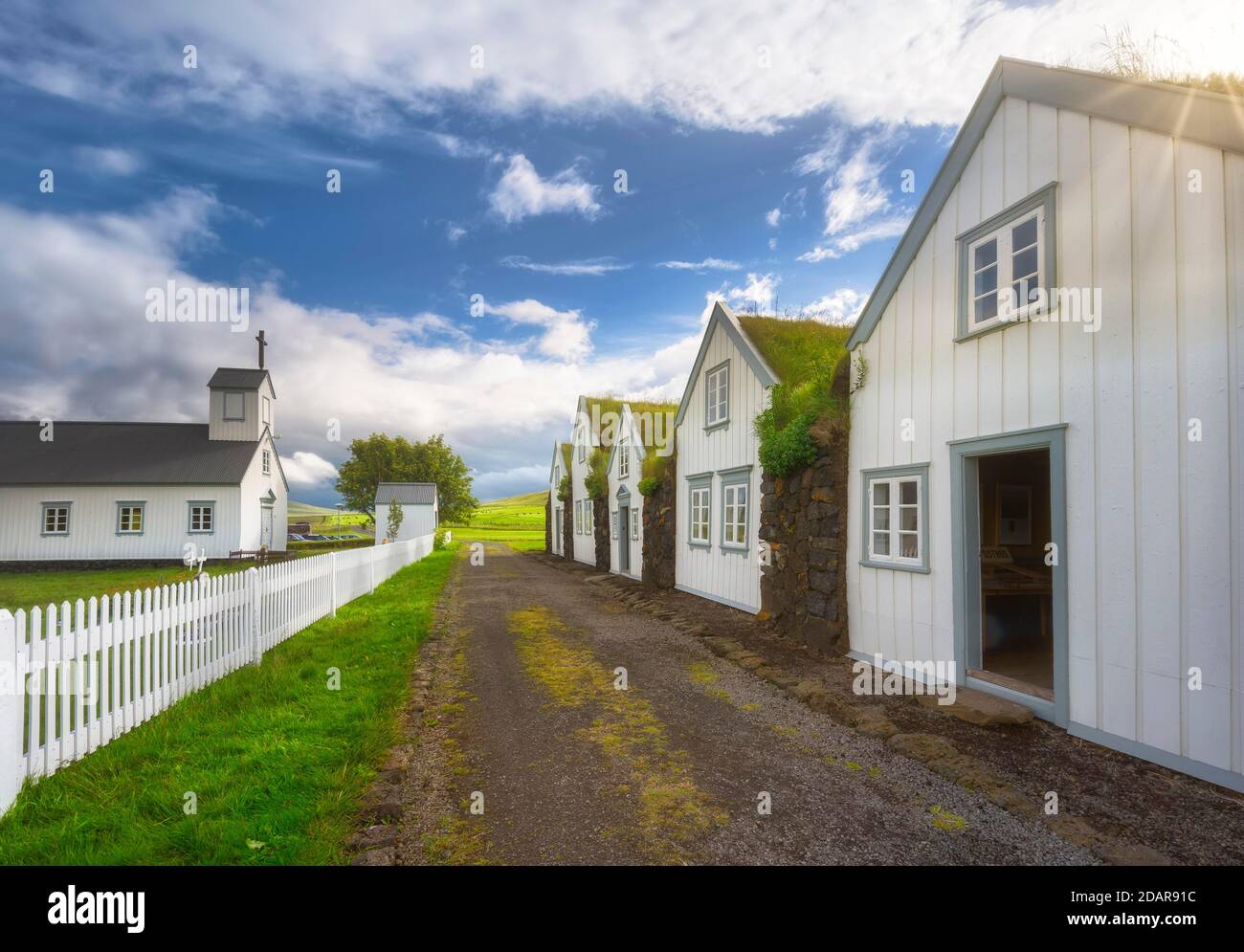 White houses with grass roof and stone wall along a gravel road, church with white fence on peat yard, grass house settlement Grenjadarstadur Stock Photo