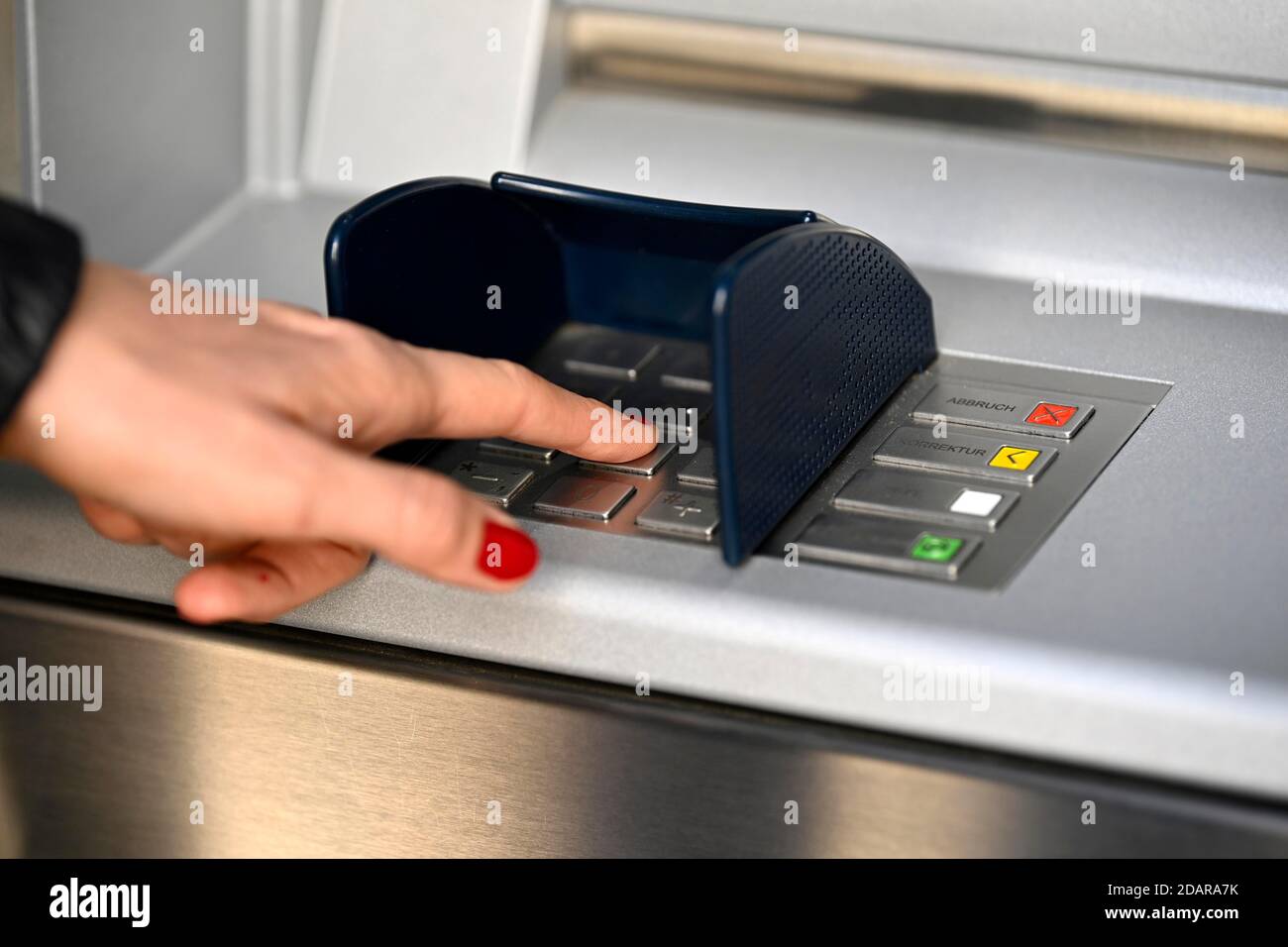 Woman typing in secret code at the cash machine of a savings bank ...