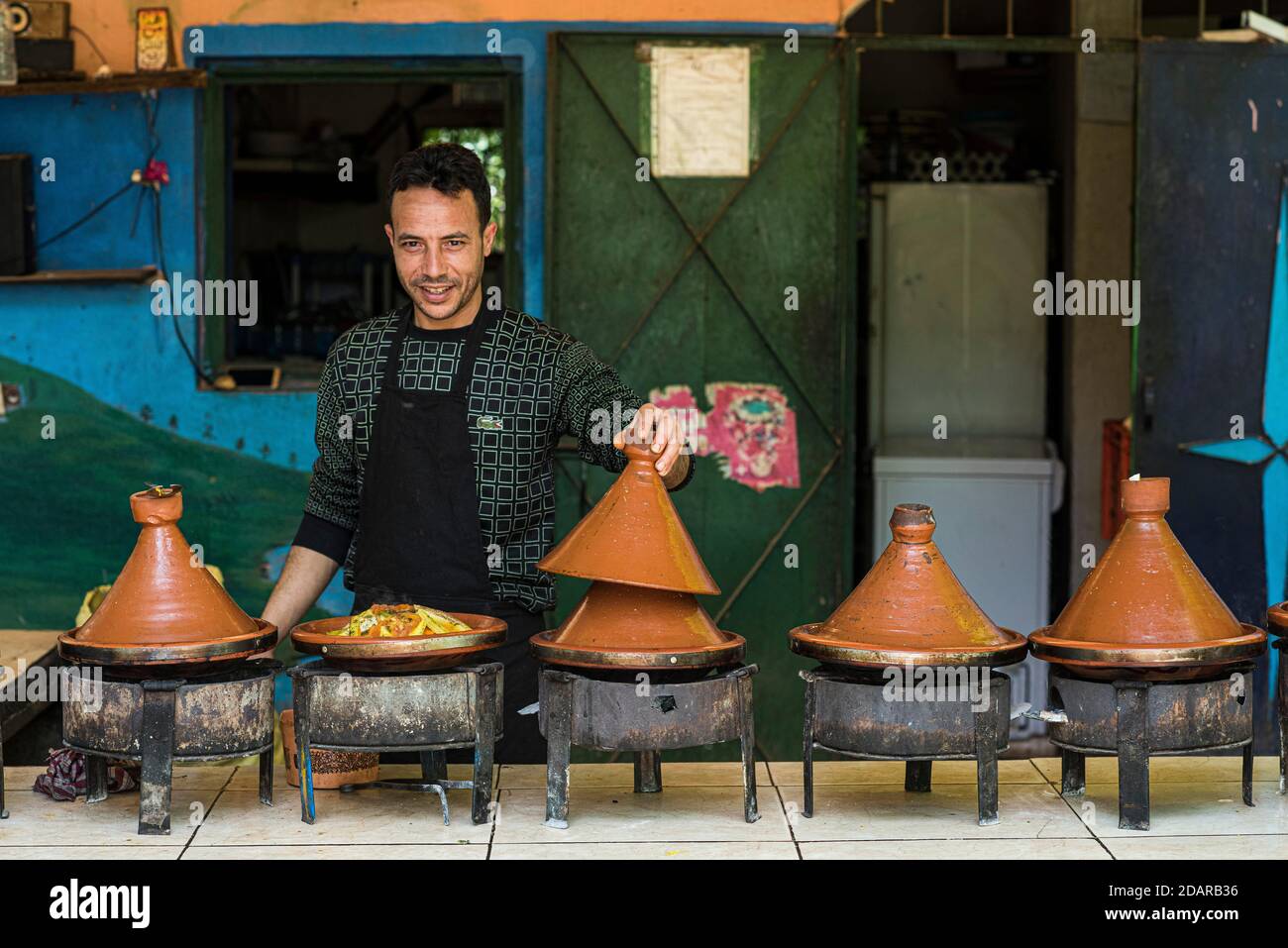 Tajine, a man offers traditional Moroccan food prepared on charcoal fire in typical Tajine pots at a stand Stock Photo