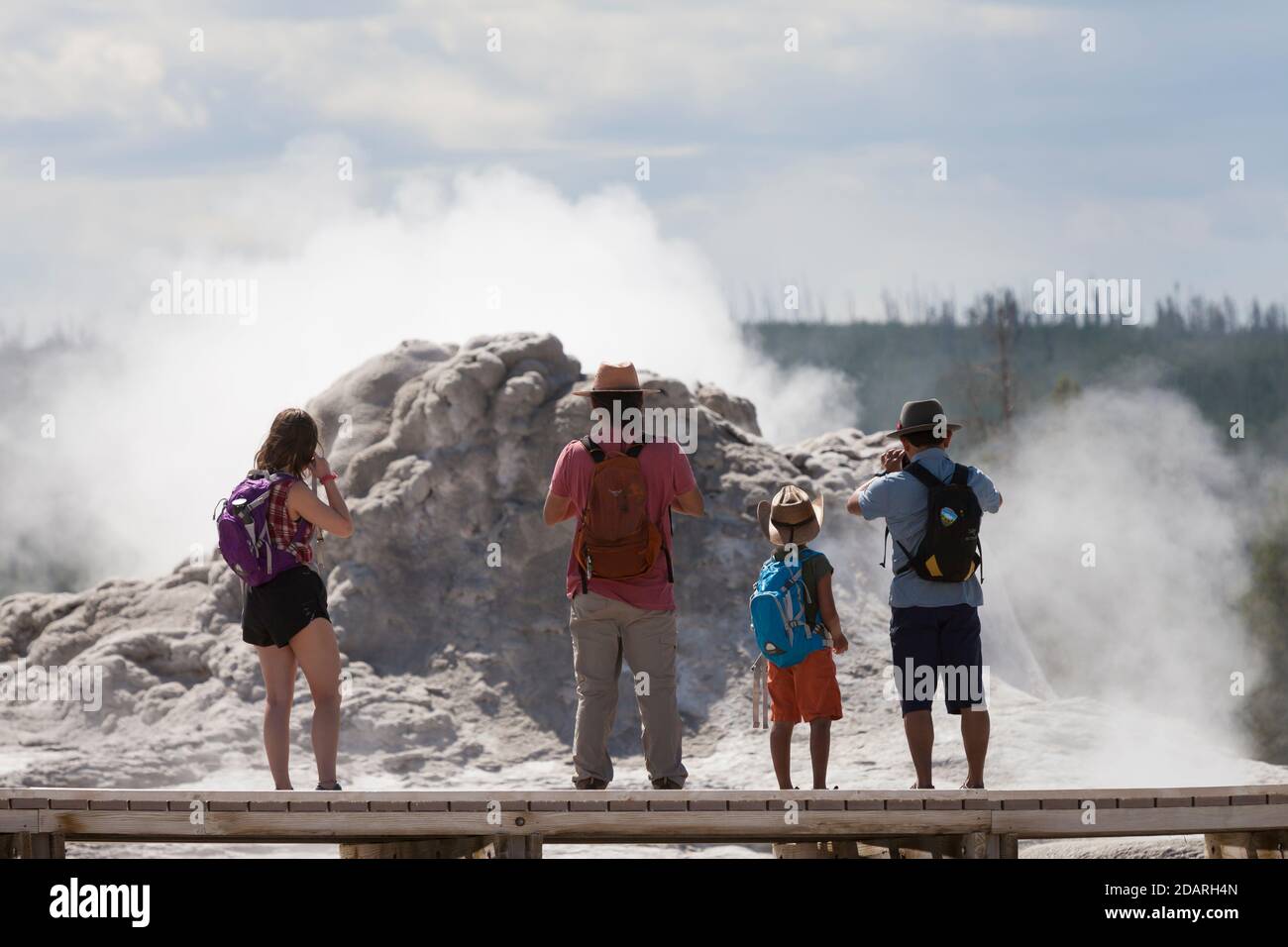 A family stops to take photos of Castle Geyser along the Upper Geyser Basin Trail in Yellowstone National Park, Wyoming on Monday, August 3, 2020. The Stock Photo
