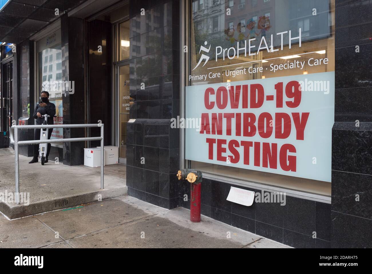 Manhattan, New York. November 13, 2020. A woman outside a clinic on 3rd avenue with a sign offering COVD-19 antibody testing. Stock Photo