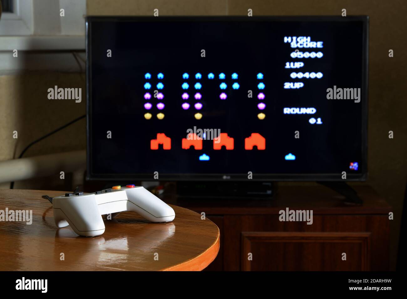 KHARKOV, UKRAINE - NOVEMBER 12, 2020: Dendy video game controller on table with Space invaders game on big display Stock Photo