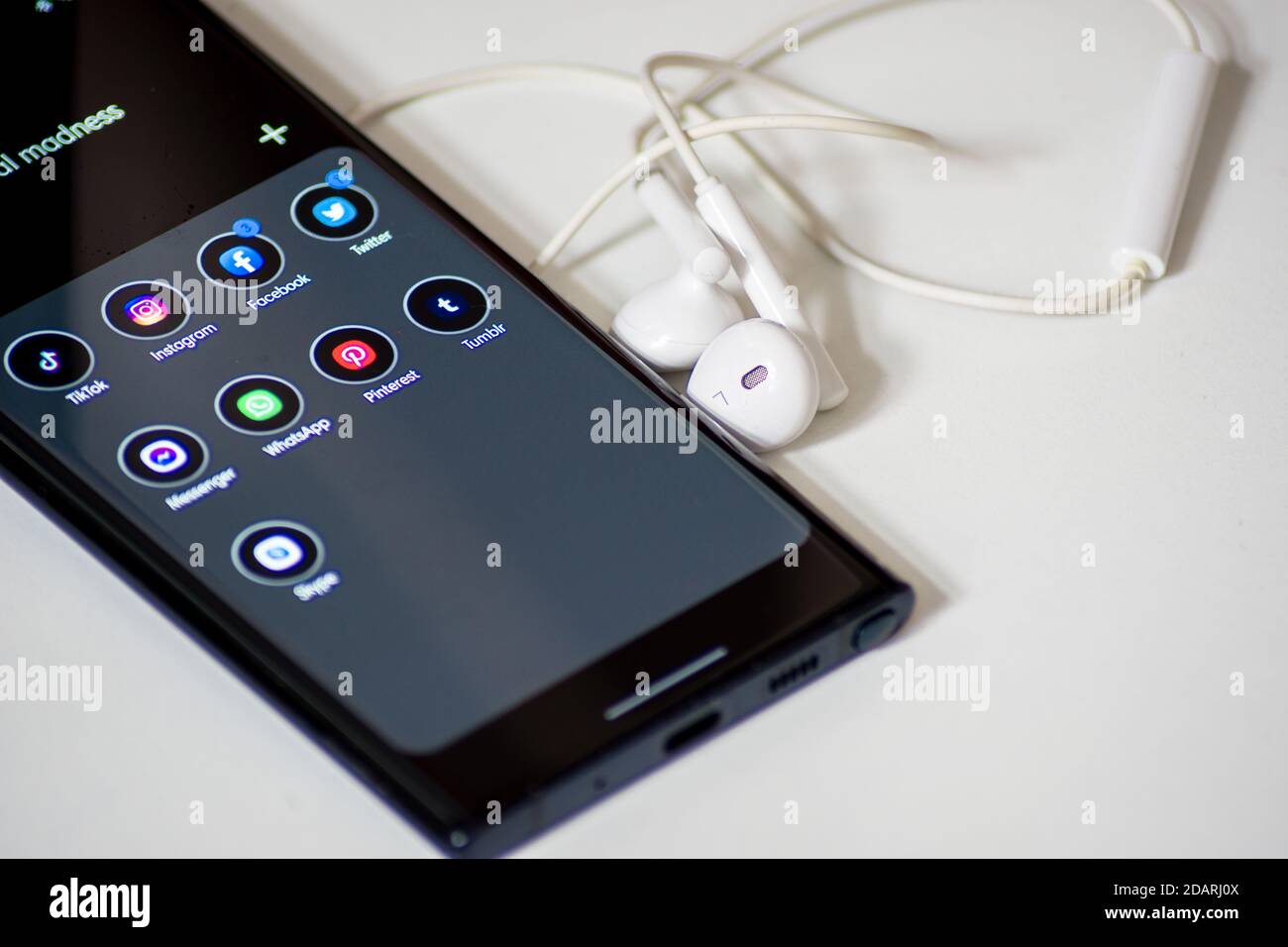 Vienna / Austria / November 13, 2020: Black smartphone with social media apps next to white earphones on the desk Stock Photo
