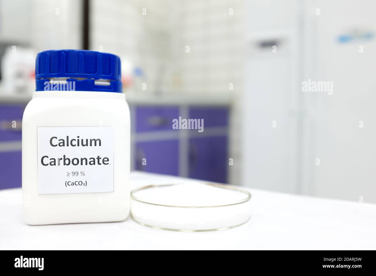 Selective focus of a bottle of calcium carbonate chemical compound or soda ash beside a petri dish with solid crystalline powder substance. Stock Photo