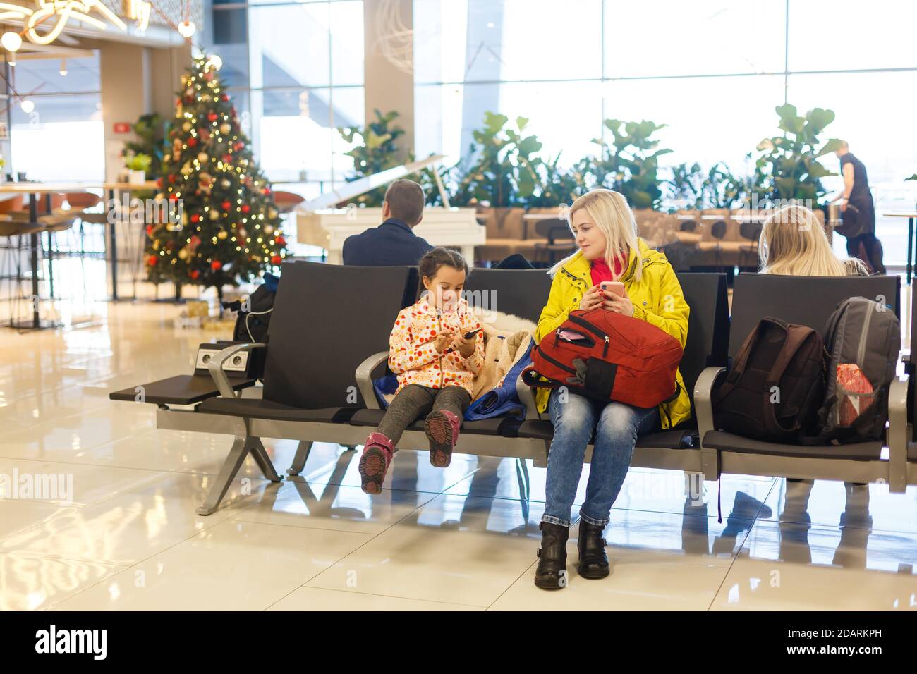 Adorable toddler girl and her mom waiting at the airport with luggage, traveling with children