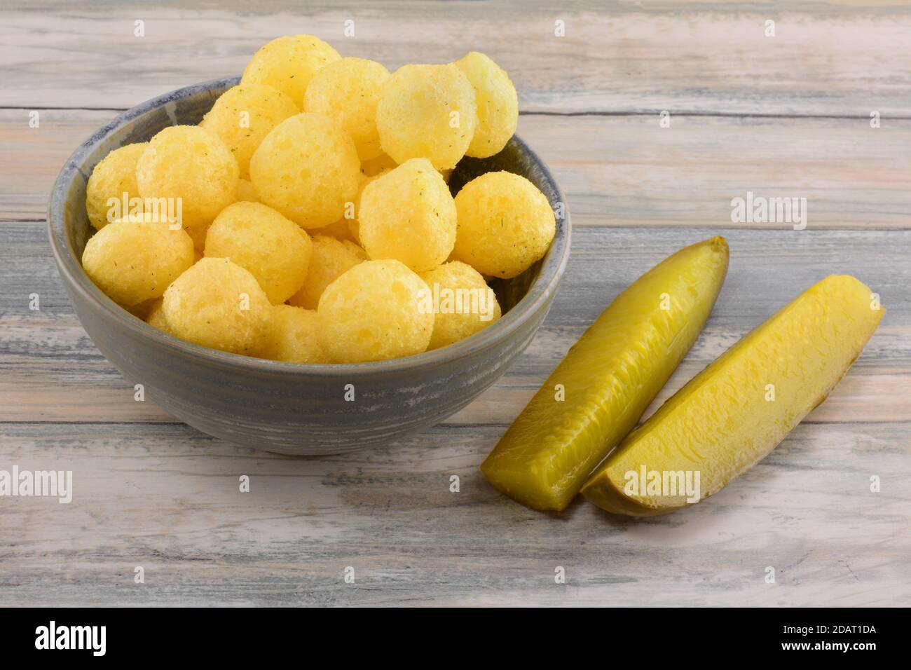 Dill pickle corn puffs in snack bowl with dill pickle spears in table