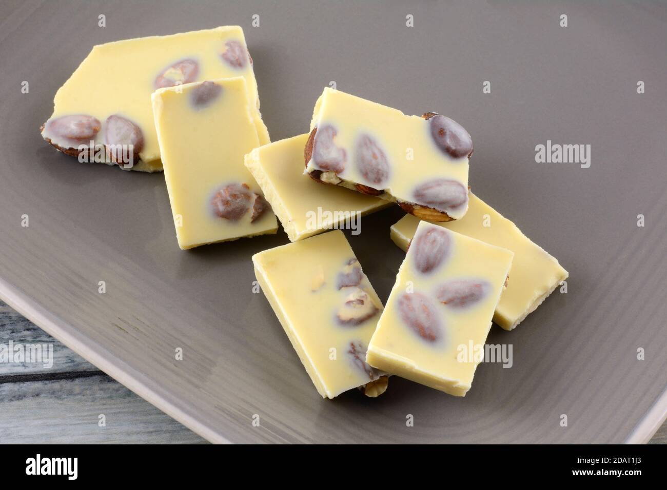 Almond white chocolate candy bar pieces with whole almond nuts on brown plate Stock Photo