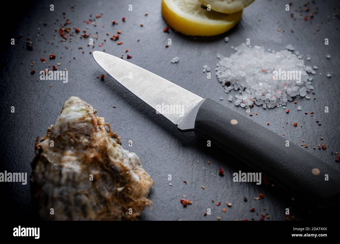 Oyster knife on on a black stone background with lemon and spices. Top view Stock Photo