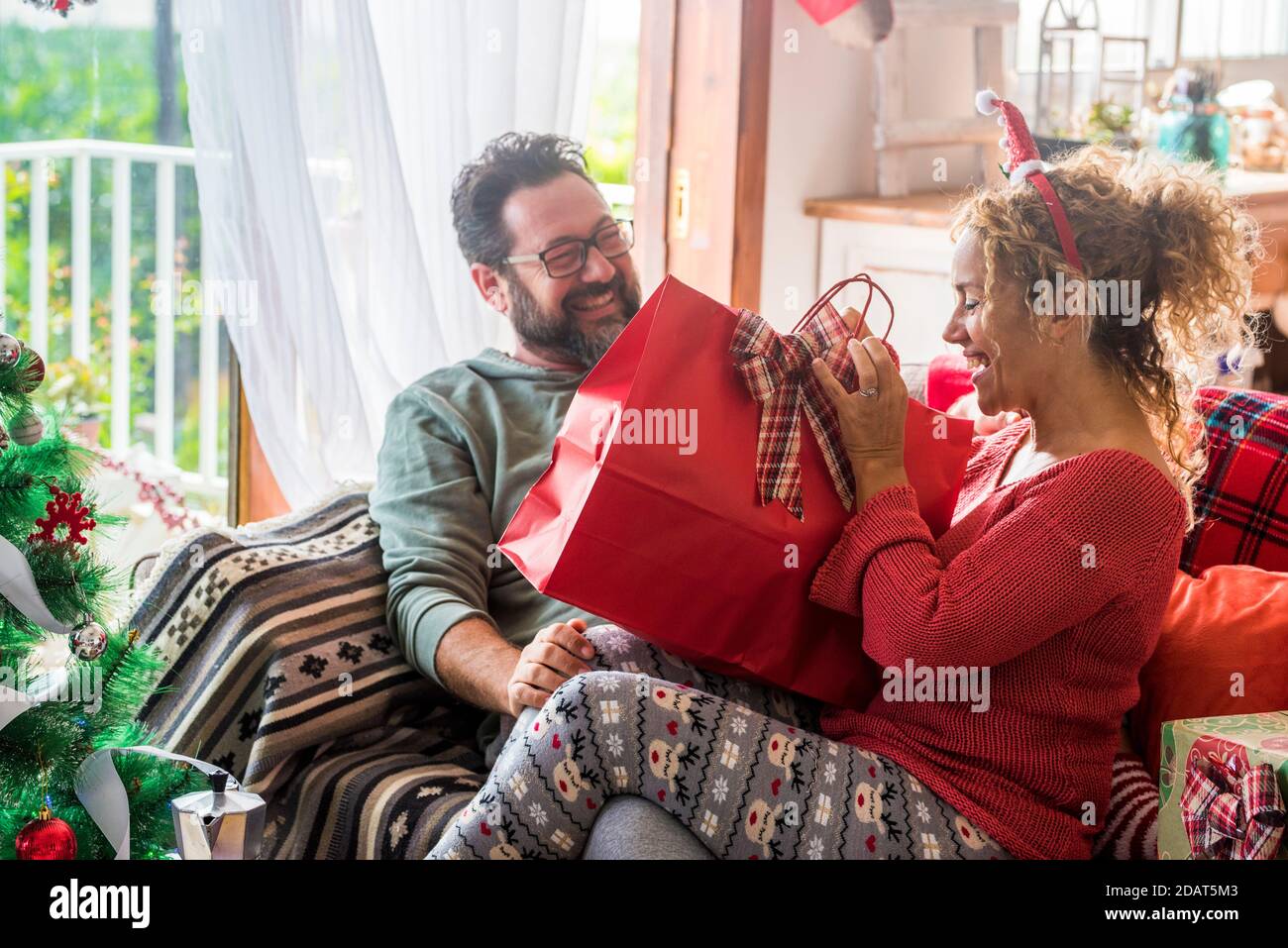 Happy couple at home enjoy christmas eve together sharing gift smiling and celebrating holidays season at home - concept of love and family share pres Stock Photo