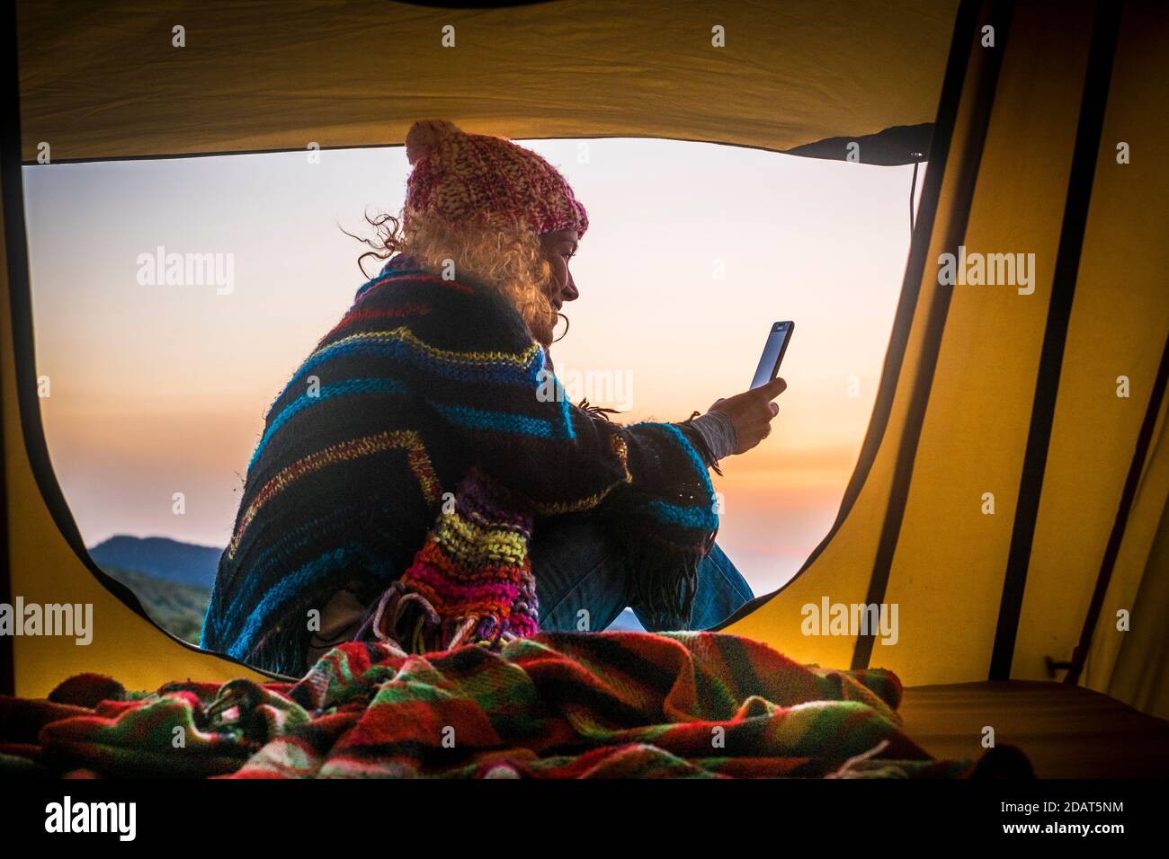 Freedom and adventure travel vacation alternative leisure activity lifestyle with woman sit down inside a tent with mountains and sunset view use smar Stock Photo