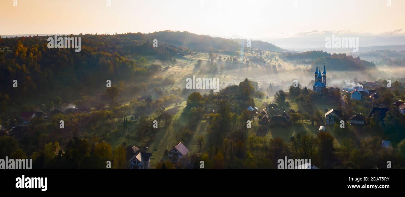Aerial view of village in fog with golden sunbeams at sunrise in autumn ...