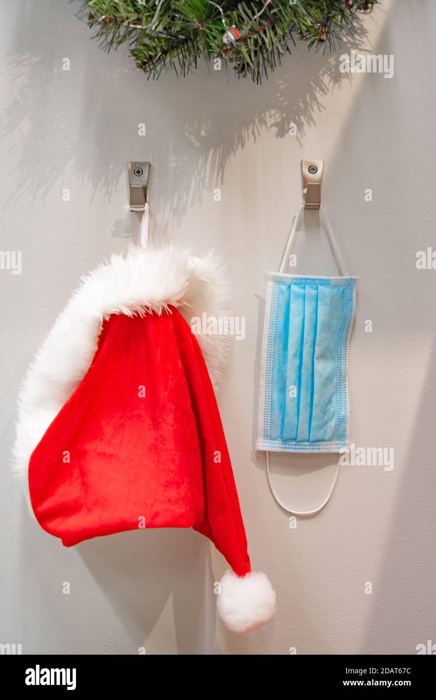 Santa Claus red and white hat and protective face mask hanging on the wall waiting to be used for delivering gifts Stock Photo