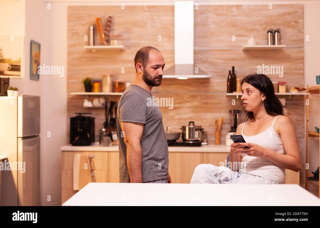 Husband suspecting wife of cheating with another man while she's texting. Frustrated offended irritated accusing woman of infidelity arguing her. Stock Photo