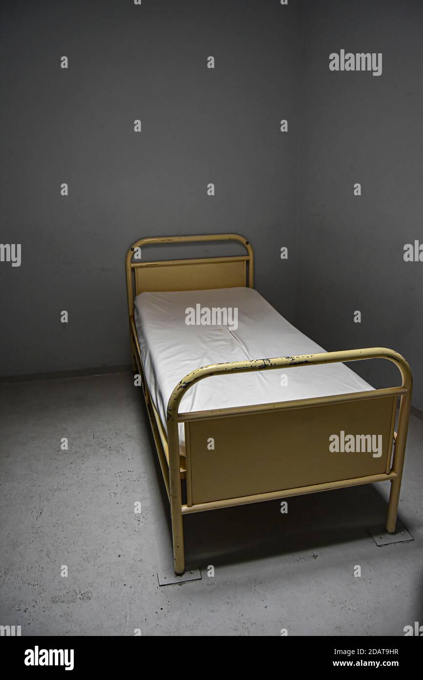 abandoned isolation cell in a hospital, hot topic in psychiatry, punishment, lonely cell, grey background with bed nailed to the ground. Stock Photo