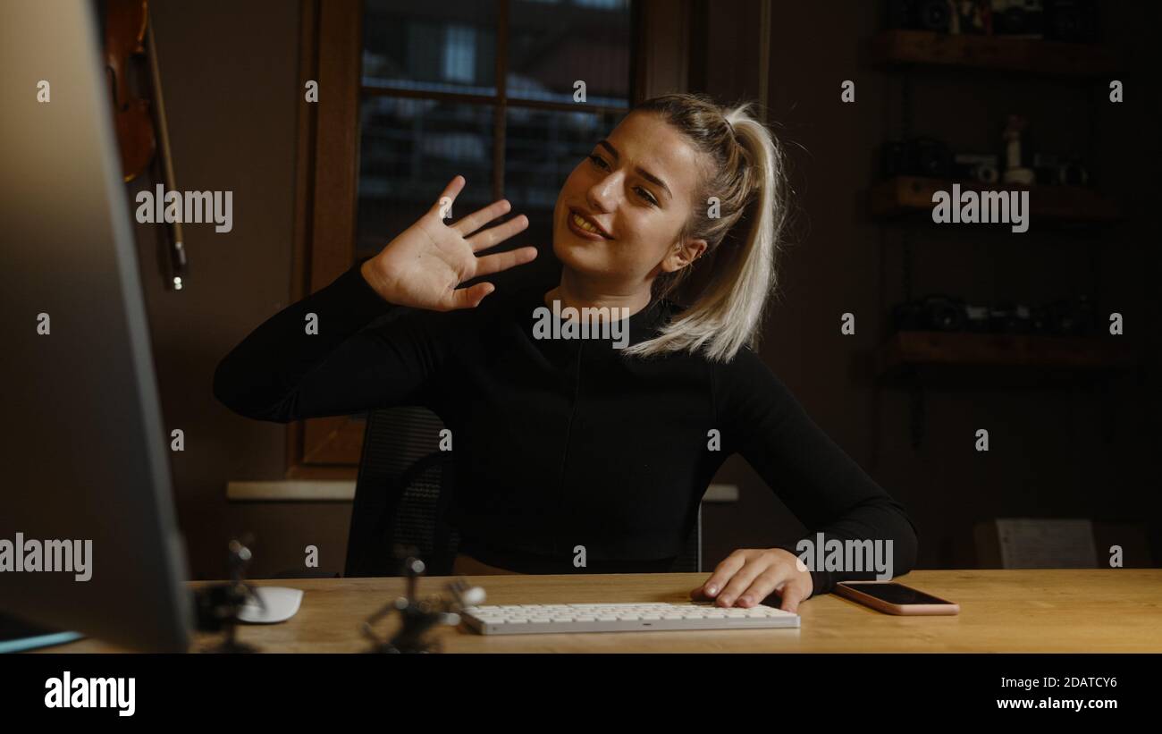 Young blonde woman in black dress is having video conference at computer in office, student and office worker concept Stock Photo