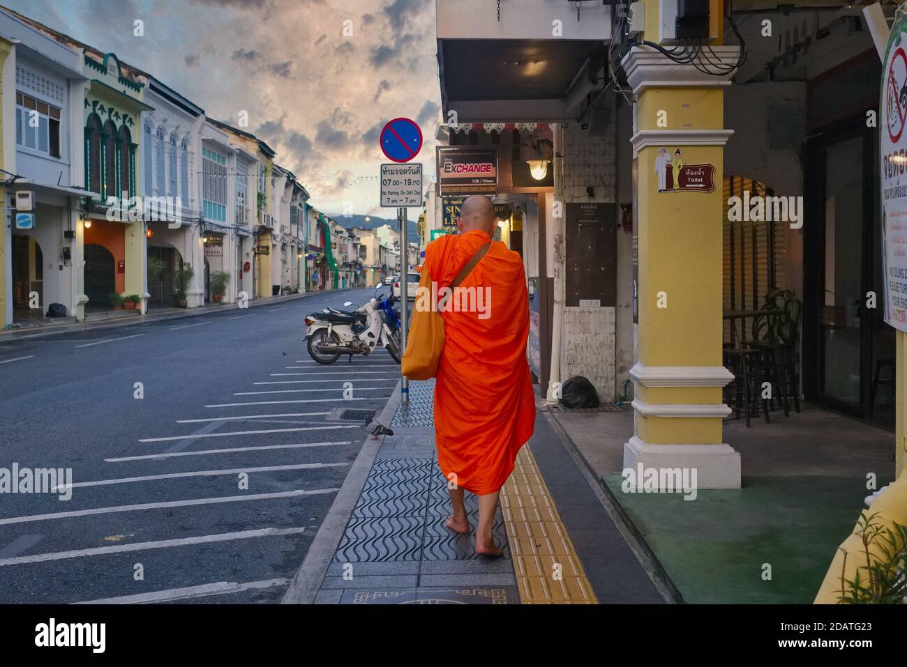 A barefoot Thai Buddhist monk walks along empty, romantic Thalang Road in the Old Town area of Phuket Town, Thailand, colourful clouds hovering above Stock Photo