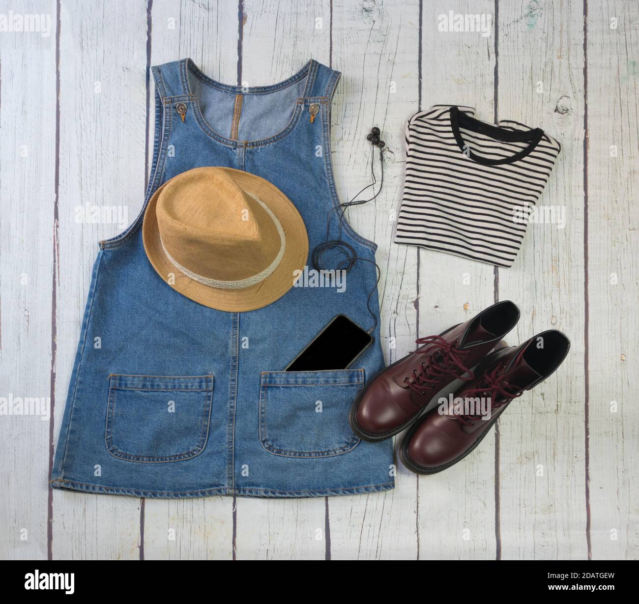 https://c8.alamy.com/comp/2DATGEW/still-life-of-clothes-denim-skirt-with-dungarees-striped-shirt-military-boots-hat-smartphone-and-headphones-on-a-white-wooden-background-2DATGEW.jpg