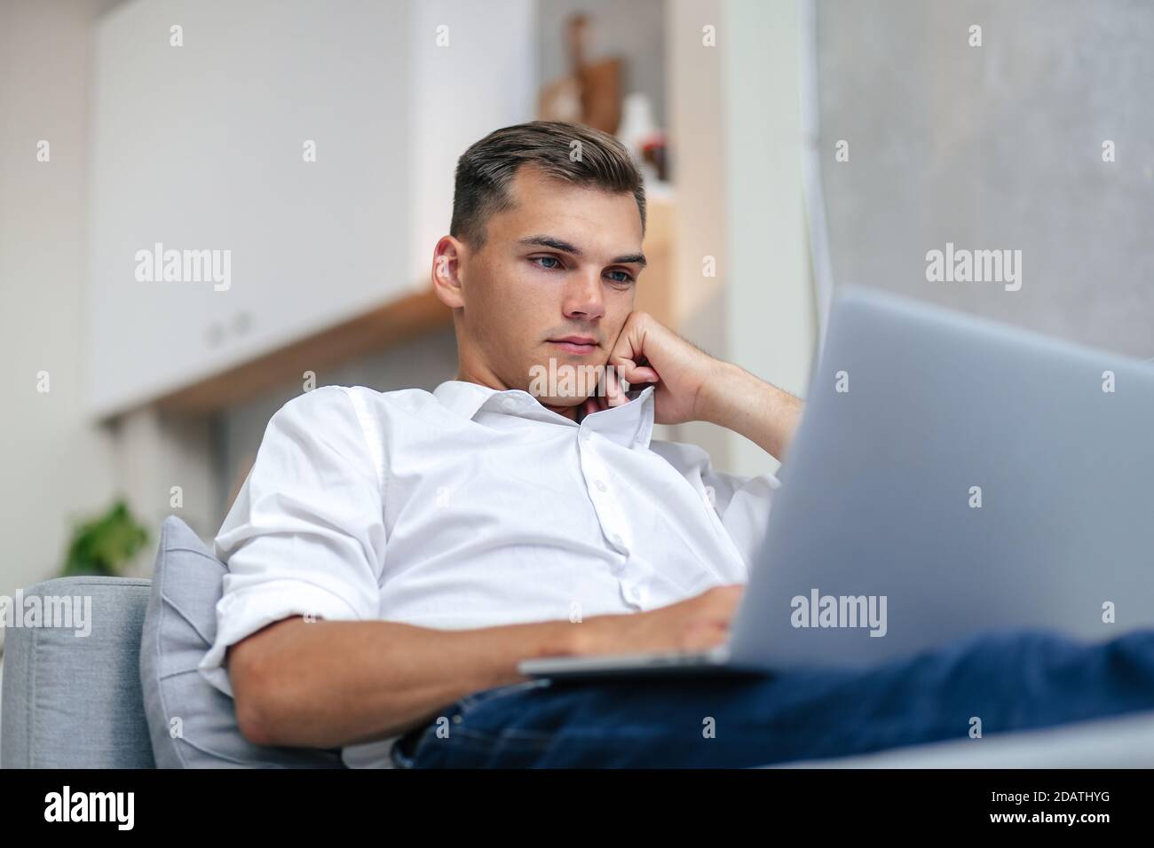 thoughtful young man browsing the Internet while lying on the couch. Stock Photo