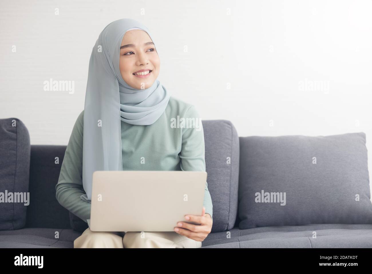 Portrait of a young happy muslim woman in hijab working at home using ...