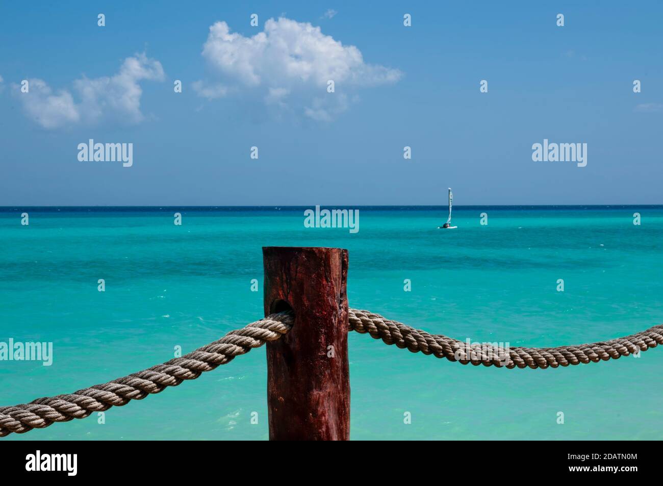 Rustic rope with a wooden support pole. In the background the Caribbean sea with a small sailboat, the blue sky and white clouds. Mexican Caribbean Stock Photo