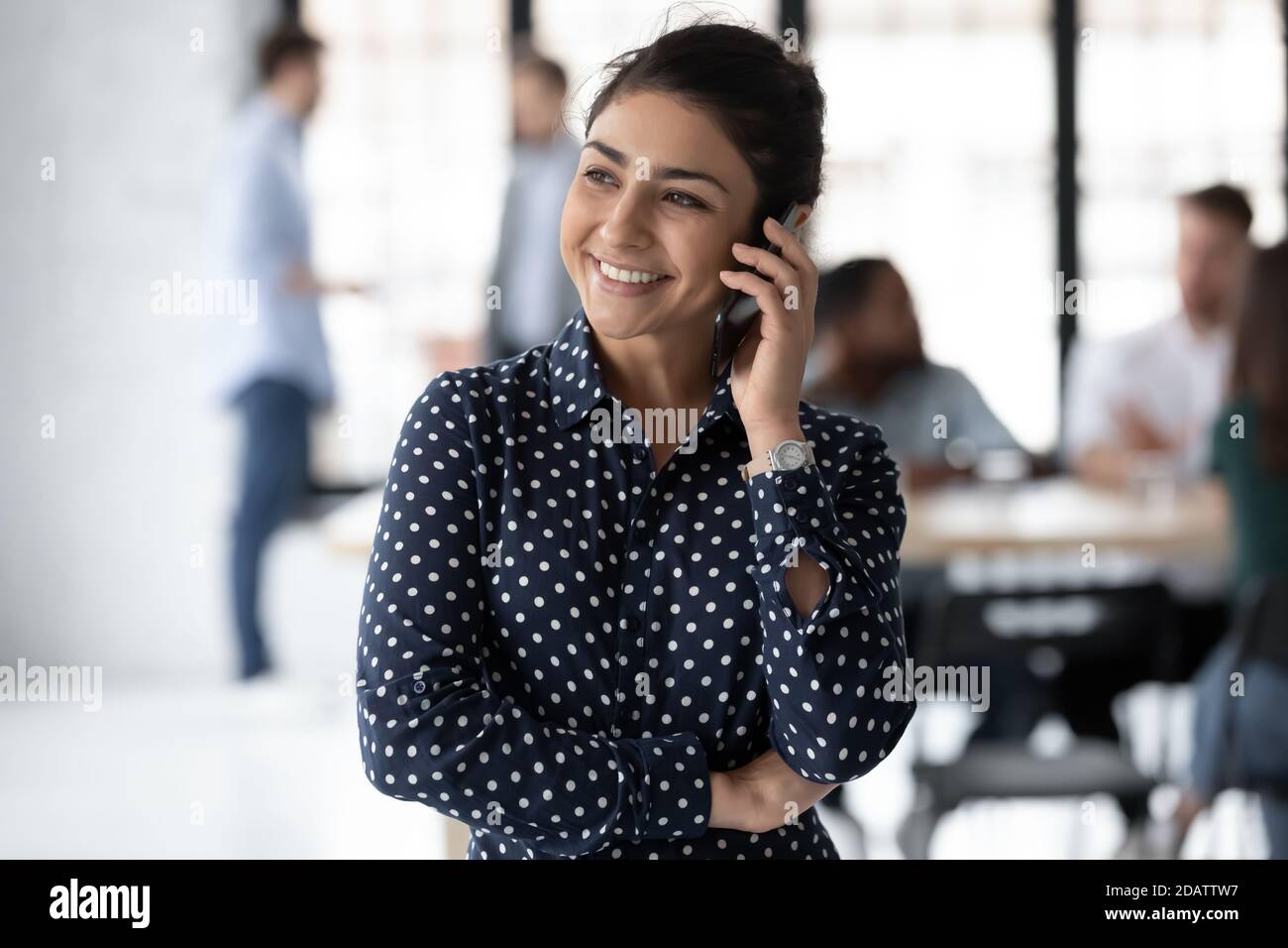 Positive indian lady consultant standing at workplace talking on phone Stock Photo