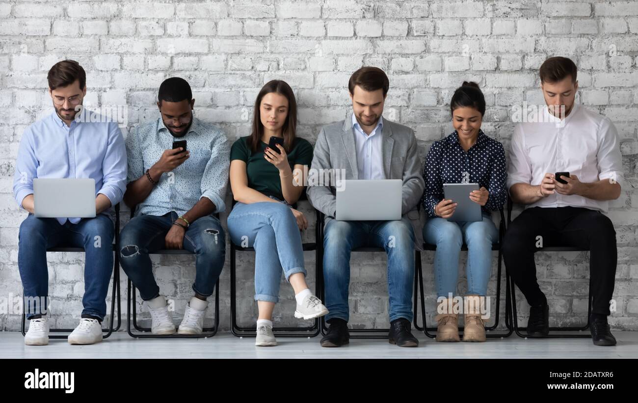 Row of diverse young people sitting by wall using gadgets Stock Photo ...