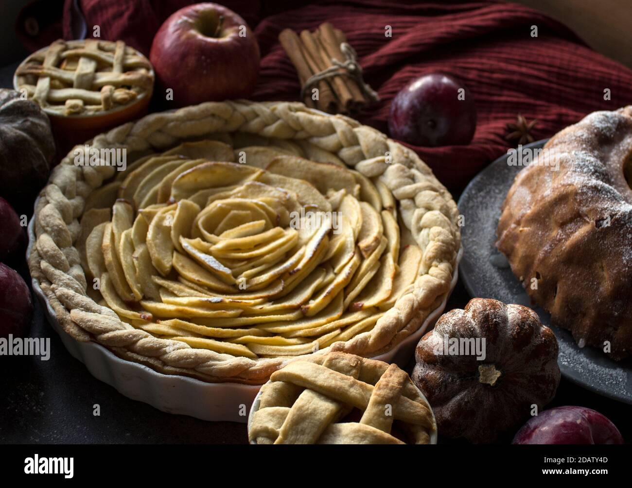 Apple pies of different types on a table with fresh fruits, cinnamon