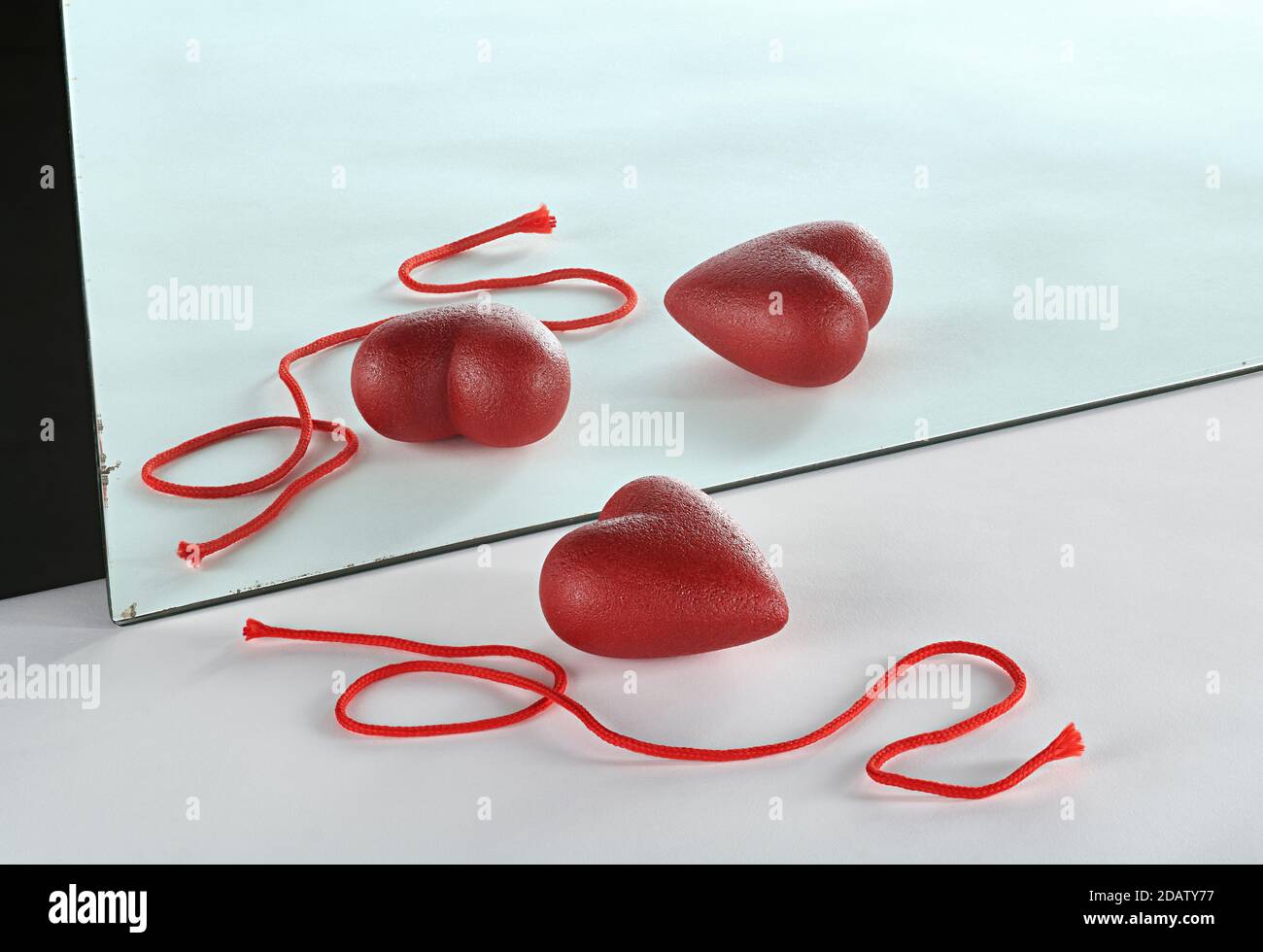 A red heart is reflected in a mirror and two hearts are seen in the reflection. Stock Photo