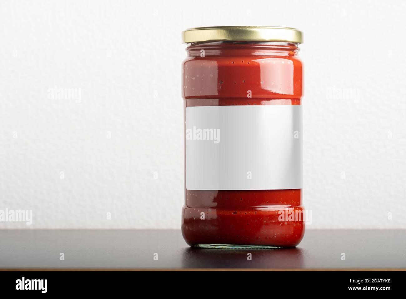 Tomato paste glassy jar with round cap on black table, editable mock-up series template ready for your design, label selection path included. Stock Photo
