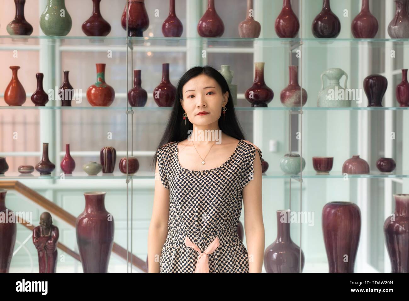 A chinese woman standing near a shelf of various vases within the walters art museum in baltimore maryland. Stock Photo