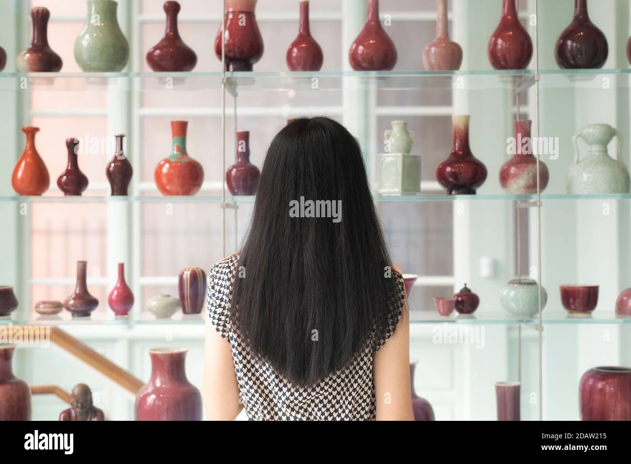 A chinese woman looking at a shelf of various vases within the walters art museum in baltimore maryland. Stock Photo