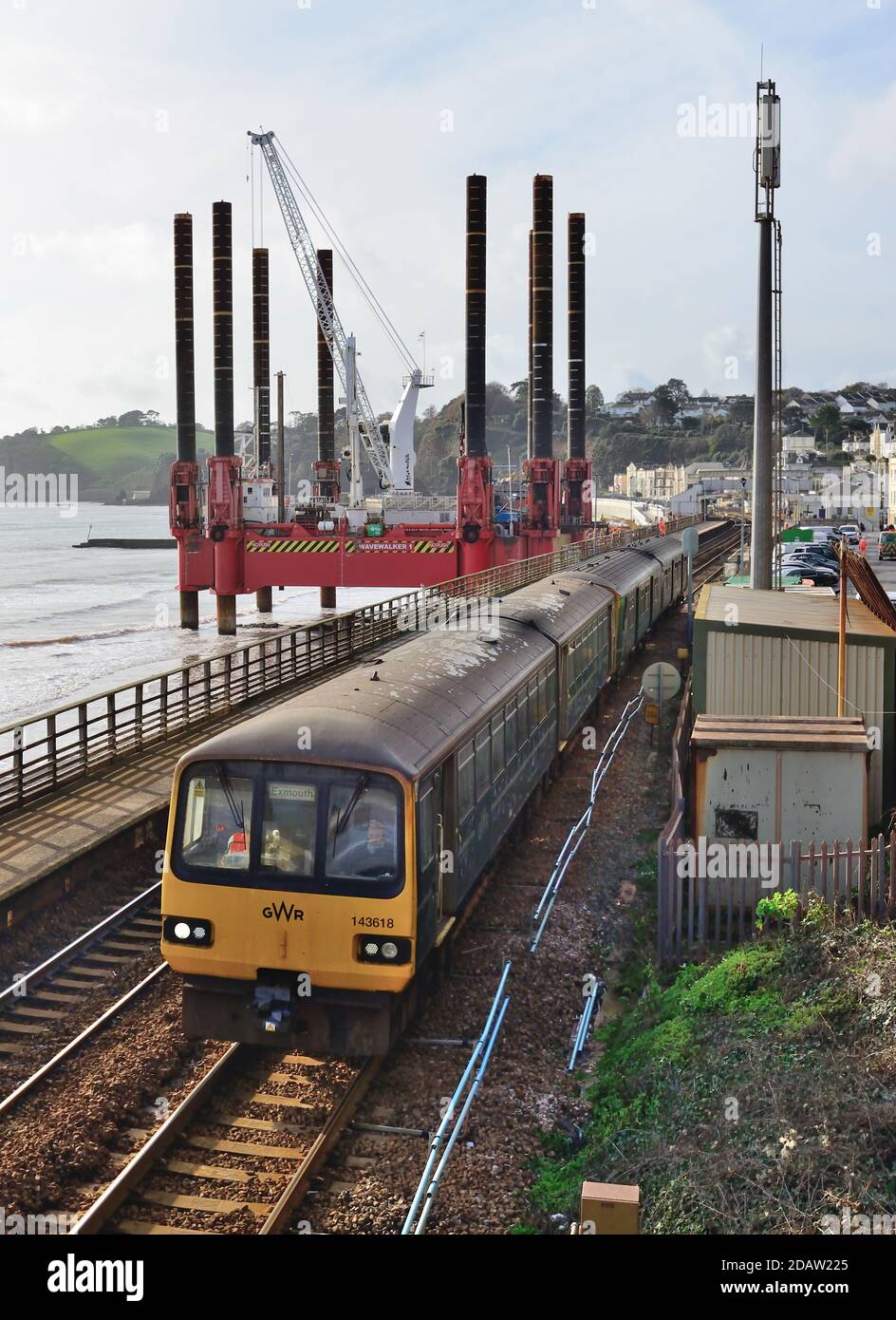 Wavewalker 1 beside Dawlish railway station during the rebuilding of the seawall, as a local train departs. (See note). Stock Photo